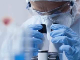 Closeup of scientist doctor looking into medical microscope analyzing blood sample
